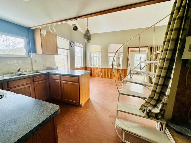 kitchen featuring a wainscoted wall, a sink, hanging light fixtures, dark countertops, and dark wood finished floors