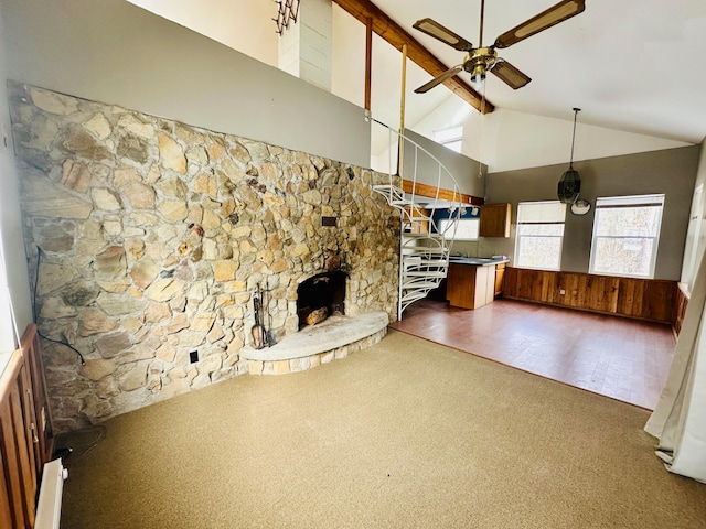 unfurnished living room with ceiling fan, dark carpet, beamed ceiling, a fireplace, and high vaulted ceiling