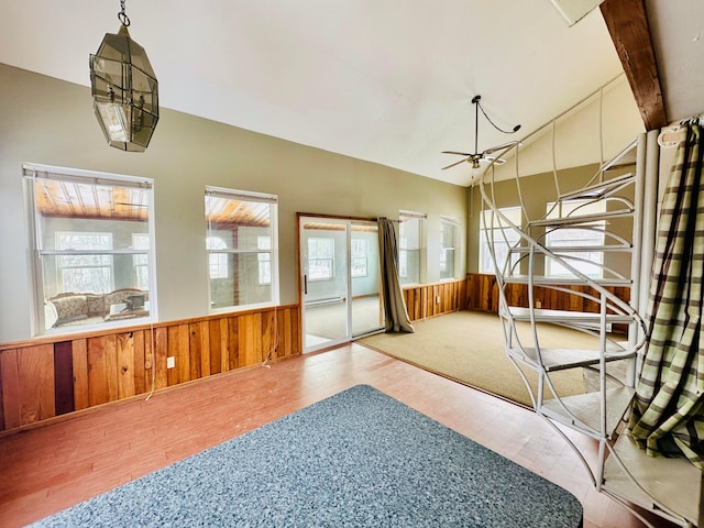 interior space with a wainscoted wall, ceiling fan, wood walls, and vaulted ceiling