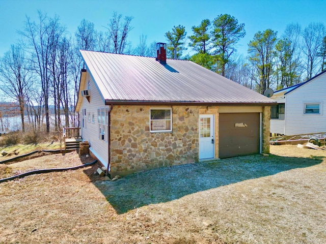 exterior space featuring metal roof, stone siding, an attached garage, and a chimney