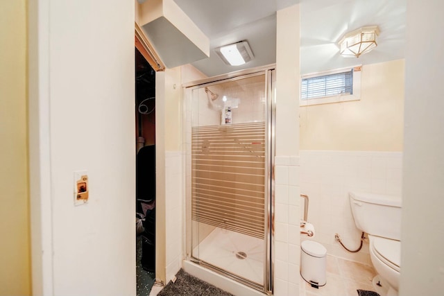 bathroom featuring tile patterned flooring, toilet, tile walls, wainscoting, and a stall shower