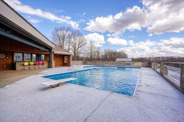 outdoor pool featuring a patio area and a diving board