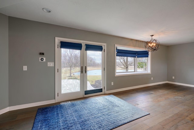 doorway to outside featuring visible vents, an inviting chandelier, hardwood / wood-style flooring, and baseboards