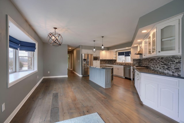 kitchen with dark countertops, a kitchen island, dark wood-style flooring, stainless steel appliances, and a sink