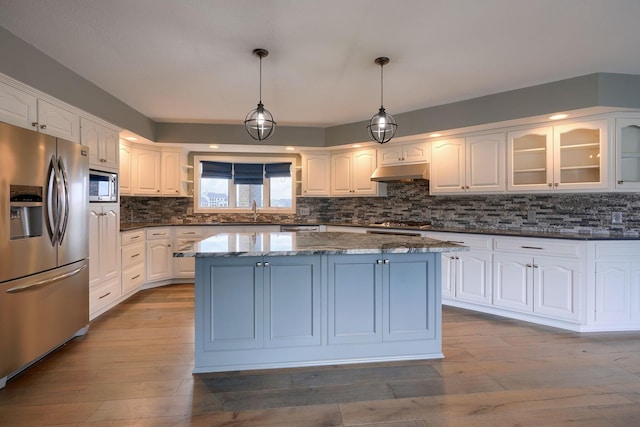 kitchen with a center island, stainless steel appliances, glass insert cabinets, white cabinets, and under cabinet range hood