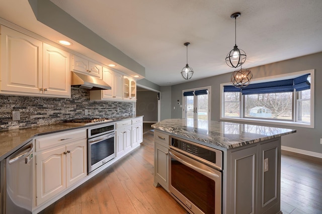 kitchen with appliances with stainless steel finishes, a healthy amount of sunlight, under cabinet range hood, and tasteful backsplash