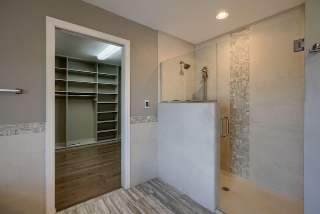 full bathroom with wood finished floors, tile walls, wainscoting, a stall shower, and a walk in closet