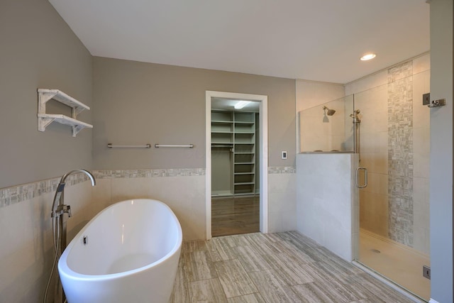 bathroom with tile walls, a freestanding bath, wainscoting, a stall shower, and a walk in closet