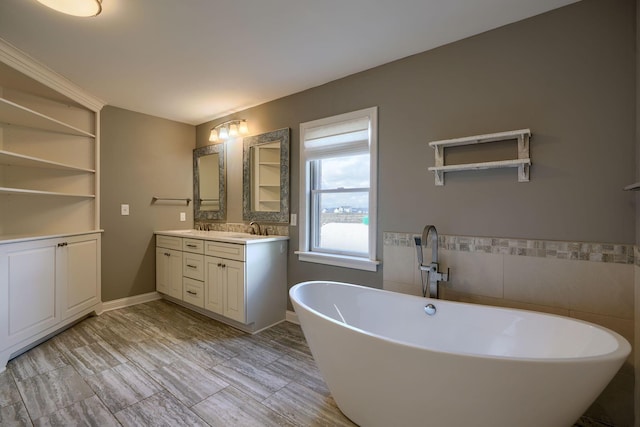 full bathroom with a sink, tile walls, a freestanding bath, and double vanity