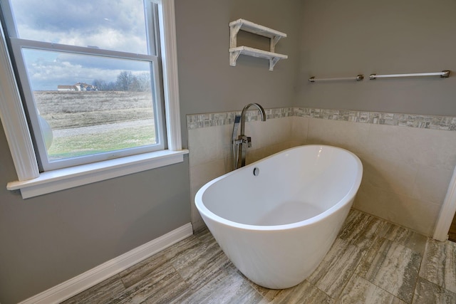 bathroom with a freestanding tub, a wainscoted wall, tile walls, and wood finished floors