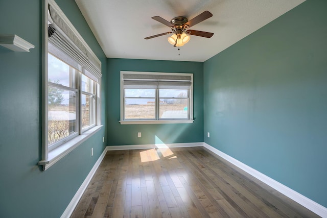 spare room featuring dark wood-type flooring, a wealth of natural light, ceiling fan, and baseboards