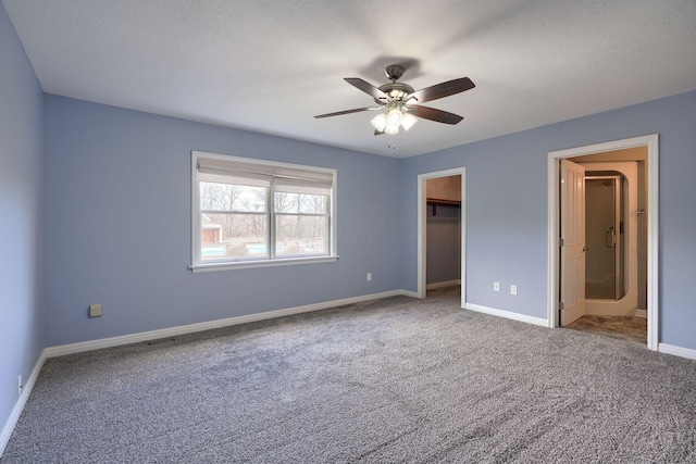 unfurnished bedroom with carpet floors, a spacious closet, baseboards, and a ceiling fan