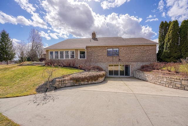 view of front of property featuring driveway, brick siding, a patio, a chimney, and a front yard