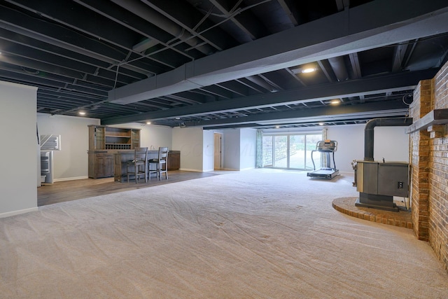 basement featuring a wood stove, baseboards, carpet floors, and a dry bar