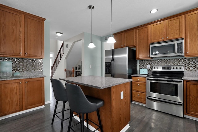 kitchen featuring dark wood-style flooring, brown cabinets, stainless steel appliances, decorative backsplash, and a kitchen island