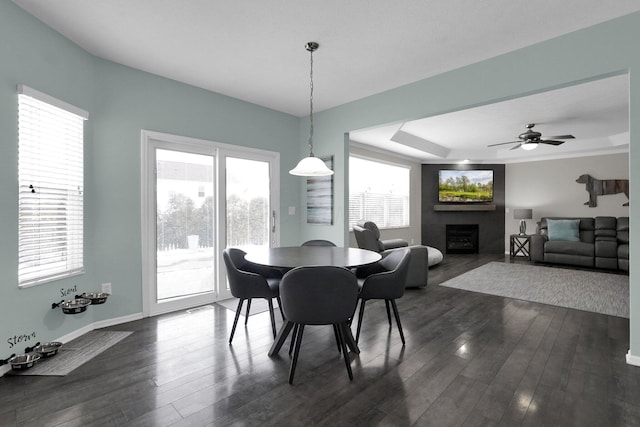 dining room with a tray ceiling, dark wood-style flooring, a fireplace, and baseboards