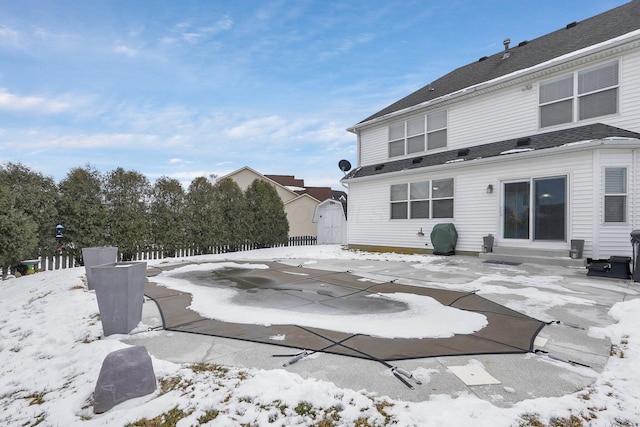 snow covered back of property featuring entry steps, an outdoor structure, and a storage unit