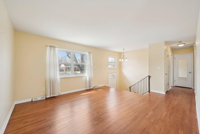 spare room with an inviting chandelier, visible vents, baseboards, and wood finished floors