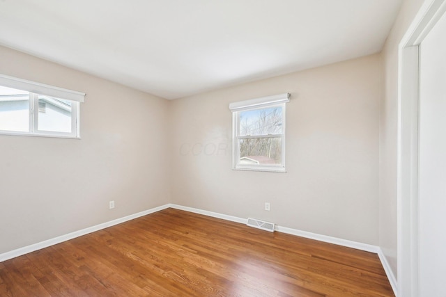 unfurnished room featuring a healthy amount of sunlight, visible vents, baseboards, and wood finished floors