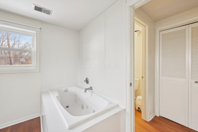 bathroom with wood finished floors, visible vents, baseboards, a closet, and a jetted tub