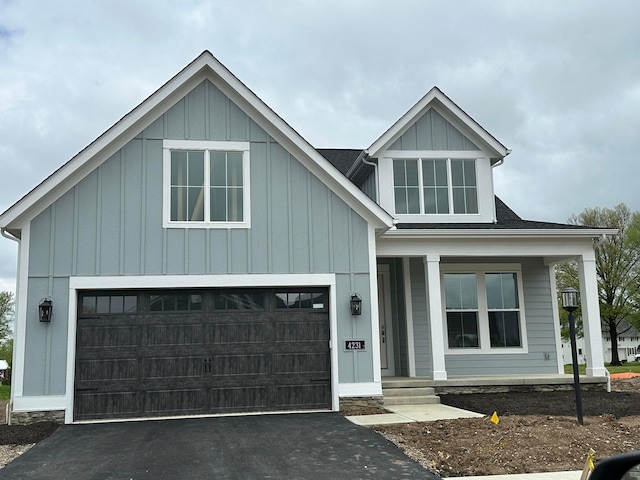 view of front facade featuring an attached garage, board and batten siding, aphalt driveway, and covered porch