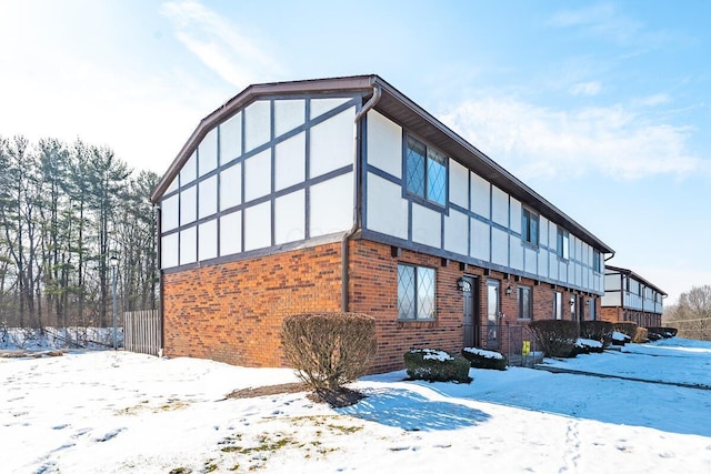 view of snowy exterior with a garage, brick siding, and stucco siding