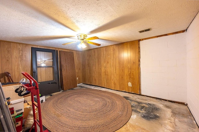 spare room with concrete block wall, visible vents, wood walls, a textured ceiling, and concrete flooring