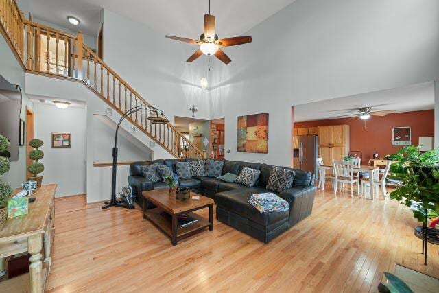 living area featuring stairs, a ceiling fan, a towering ceiling, and light wood-style floors