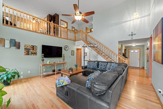 living area featuring ceiling fan, stairs, a high ceiling, and wood finished floors