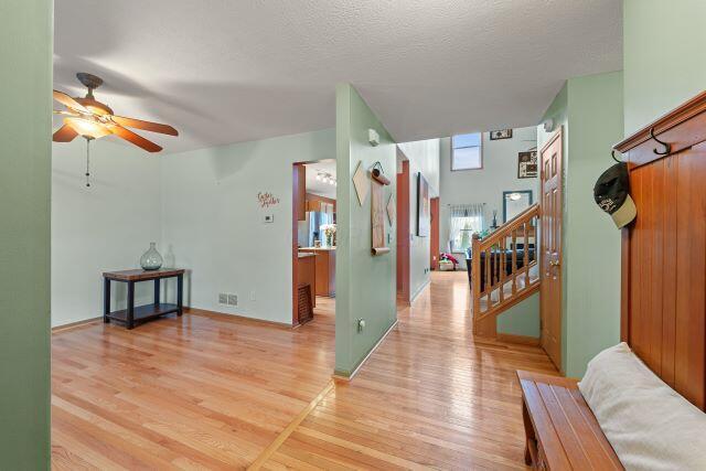 foyer entrance with light wood finished floors, baseboards, a ceiling fan, stairs, and a textured ceiling