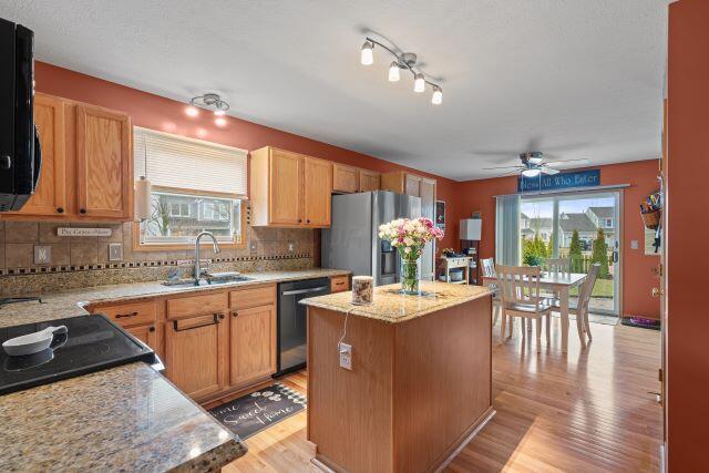 kitchen with a kitchen island, a sink, light stone countertops, stainless steel fridge, and dishwasher