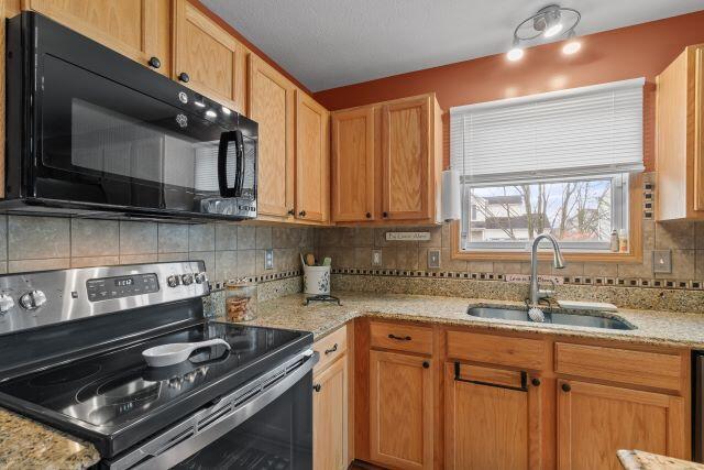 kitchen featuring tasteful backsplash, light stone counters, stainless steel electric range, black microwave, and a sink