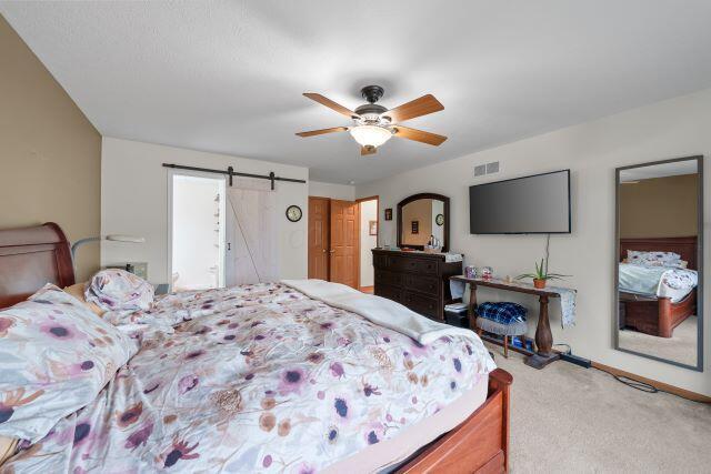 bedroom featuring a barn door, visible vents, ceiling fan, and carpet flooring