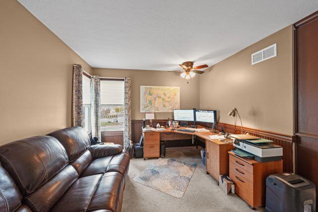 office featuring light colored carpet, wainscoting, visible vents, and ceiling fan