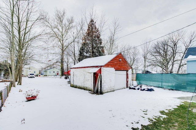 snowy yard with a garage, an outdoor structure, and fence