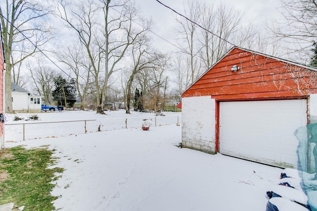 snowy yard featuring fence, a detached garage, and an outdoor structure