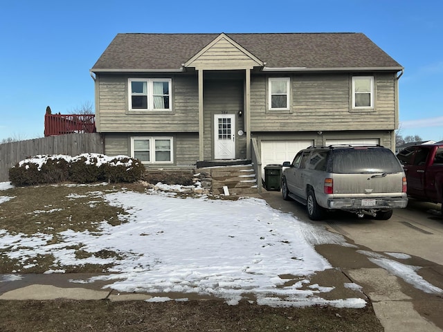 bi-level home with a garage, driveway, a shingled roof, and fence