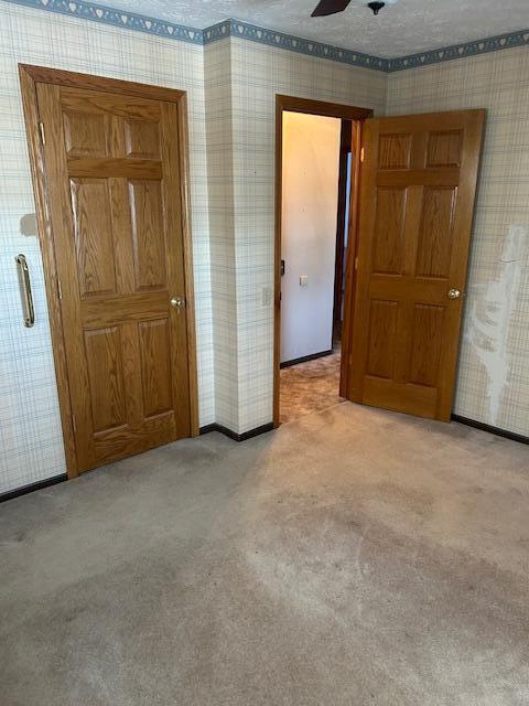 unfurnished bedroom featuring light carpet, wallpapered walls, baseboards, ceiling fan, and a textured ceiling