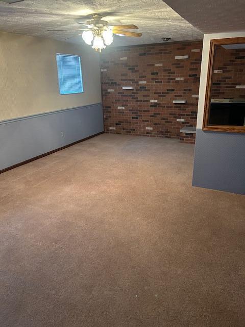 interior space with a textured ceiling, ceiling fan, carpet, and brick wall