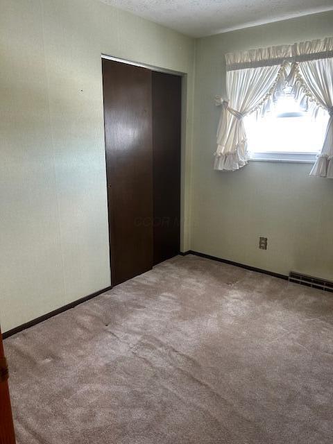 unfurnished bedroom with visible vents, a closet, light carpet, and a textured ceiling