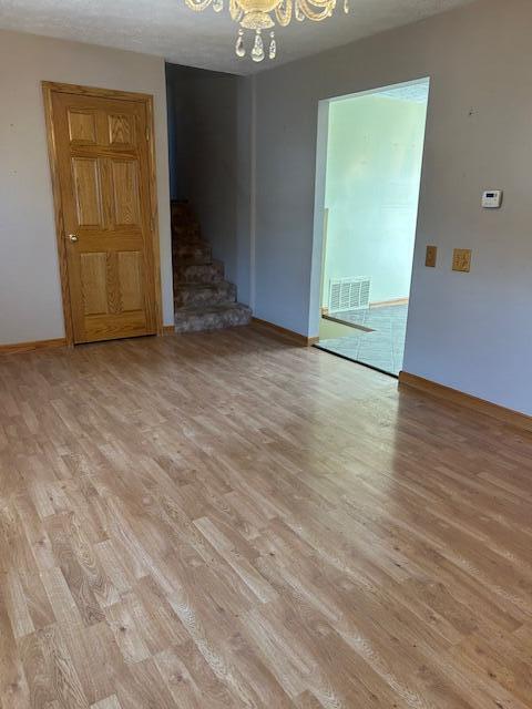 spare room featuring light wood-style flooring, visible vents, stairway, and a chandelier