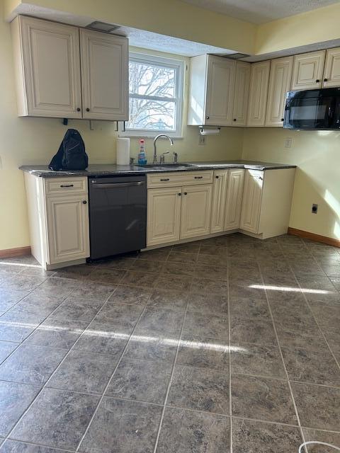 kitchen featuring dark countertops, baseboards, a sink, and black appliances