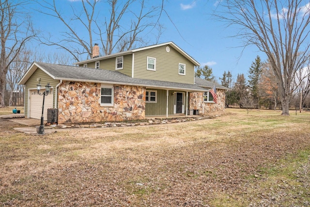 back of house with a porch, an attached garage, stone siding, a yard, and a chimney