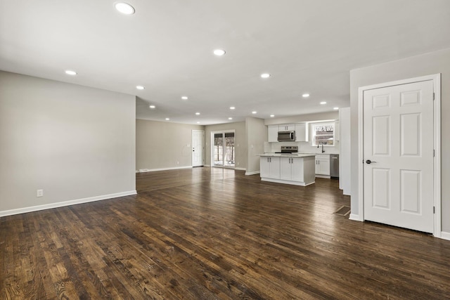 unfurnished living room featuring dark wood-style floors, recessed lighting, baseboards, and a sink