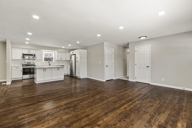 unfurnished living room featuring dark wood finished floors, recessed lighting, baseboards, and a sink