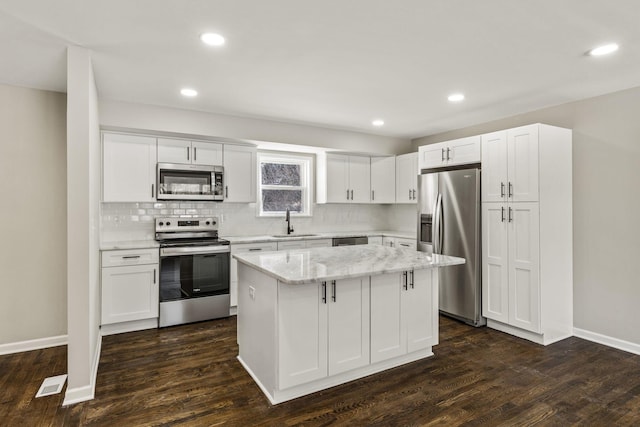 kitchen featuring tasteful backsplash, a kitchen island, dark wood finished floors, stainless steel appliances, and a sink