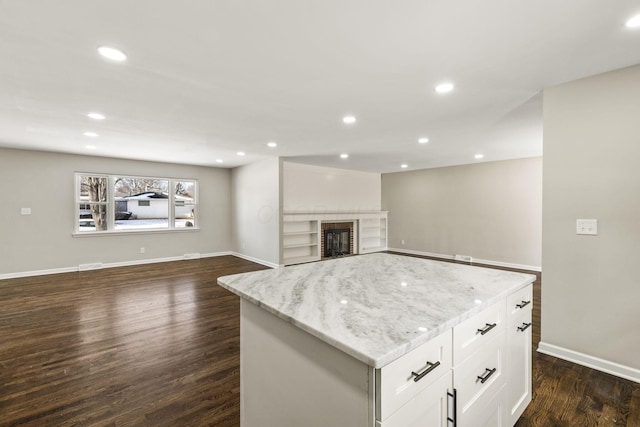 kitchen featuring light stone countertops, dark wood-type flooring, white cabinetry, a brick fireplace, and open floor plan