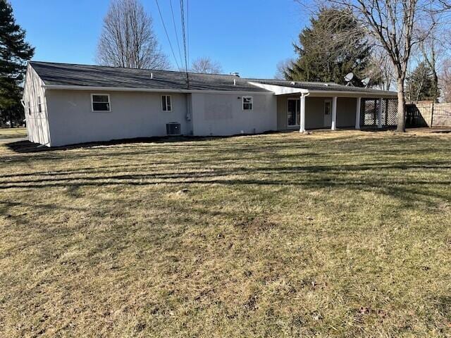 rear view of house with stucco siding, central AC, a yard, and fence