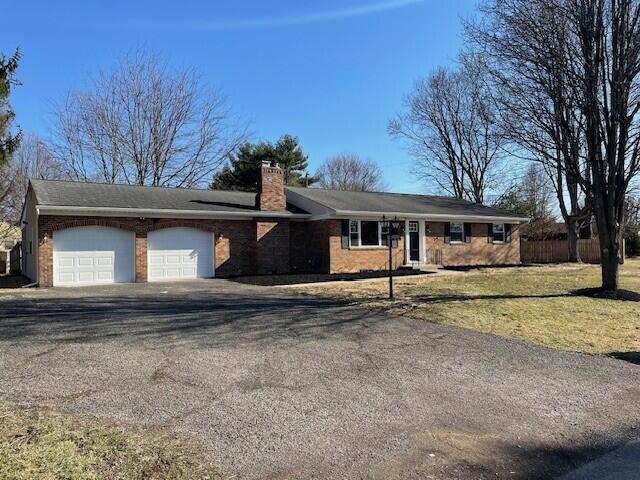 ranch-style house with a front lawn, aphalt driveway, fence, brick siding, and a chimney