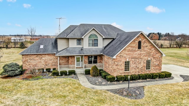 traditional-style house featuring a porch, a front yard, and brick siding